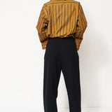 woman in black pants and golden blouse standing in front of a white wall