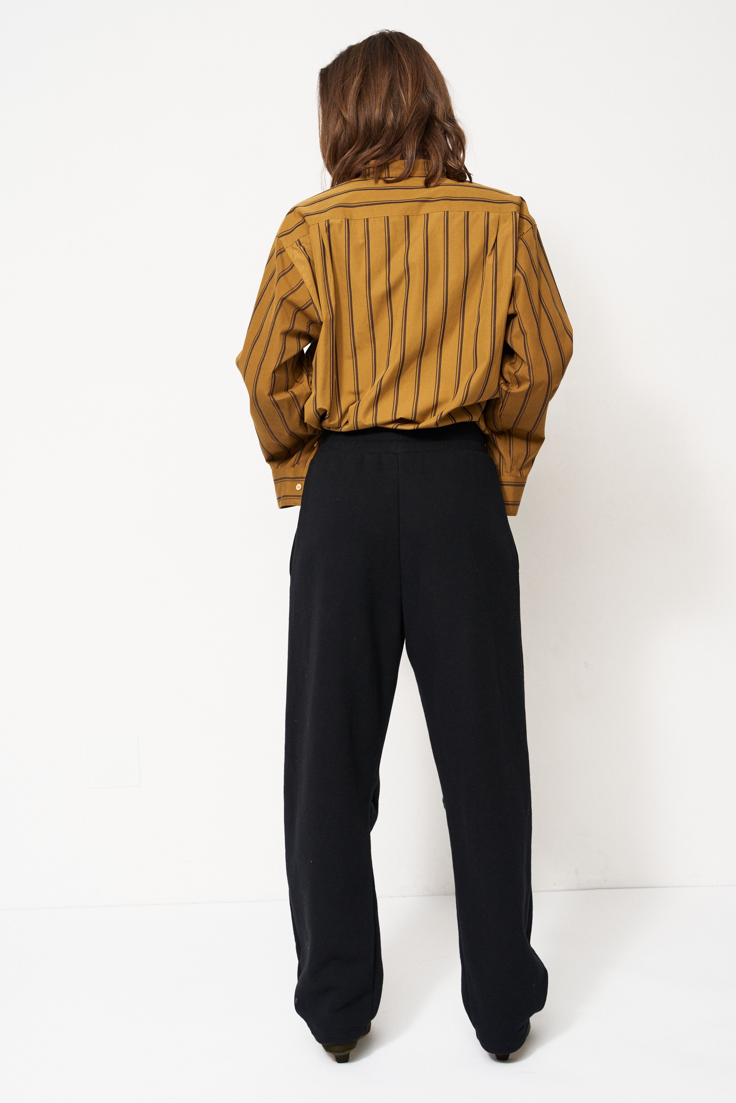 woman in black pants and golden blouse standing in front of a white wall