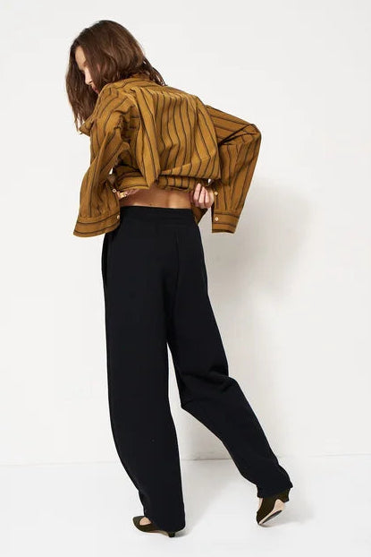 woman in gold blouse and black trackpant in front of a white wall