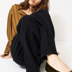 woman in black pants and golden blouse standing in front of a white wall