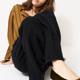 woman in black pants and golden blouse standing in front of a white wall