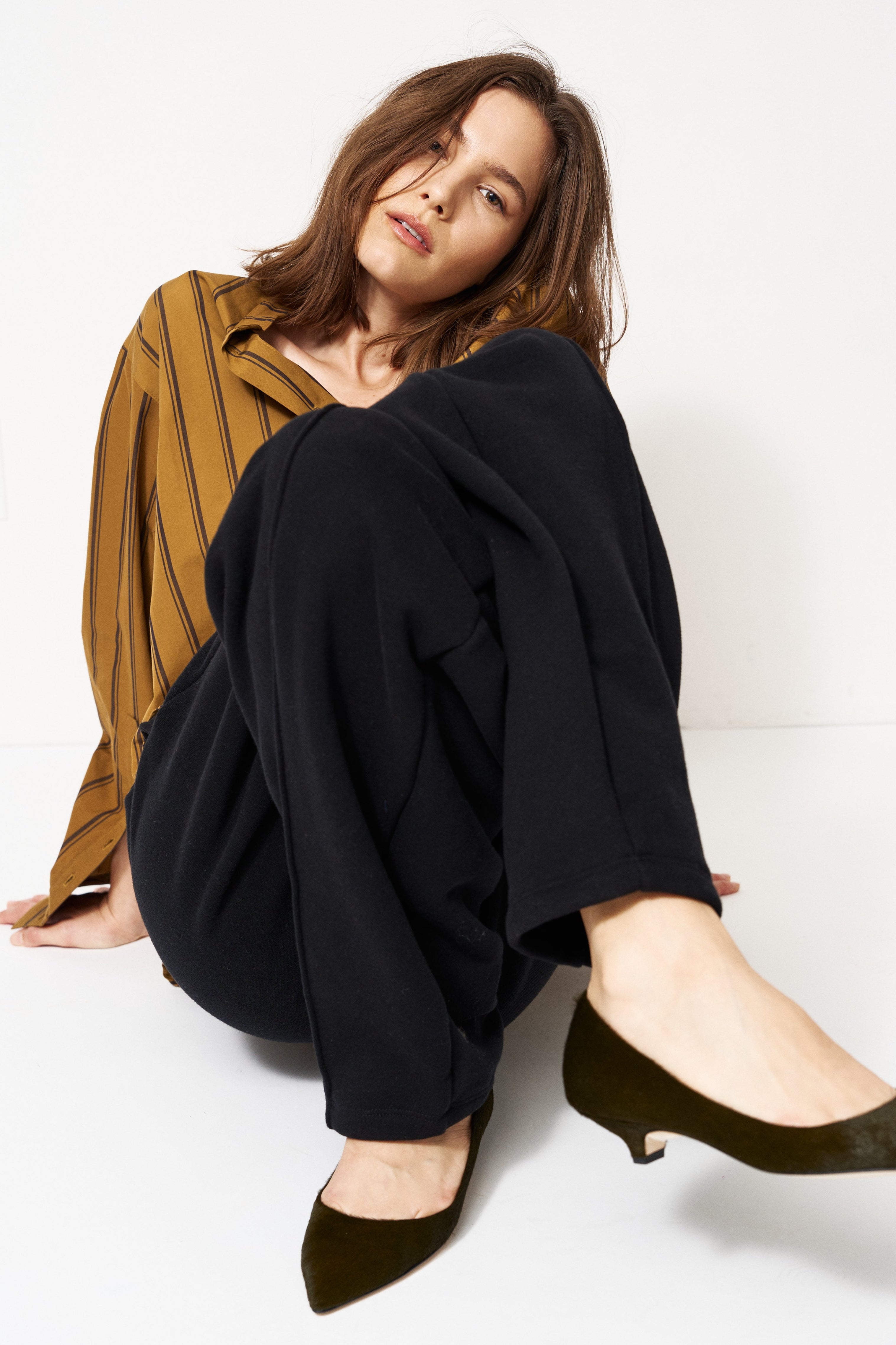woman in black pants and golden blouse standing in front of a white wall