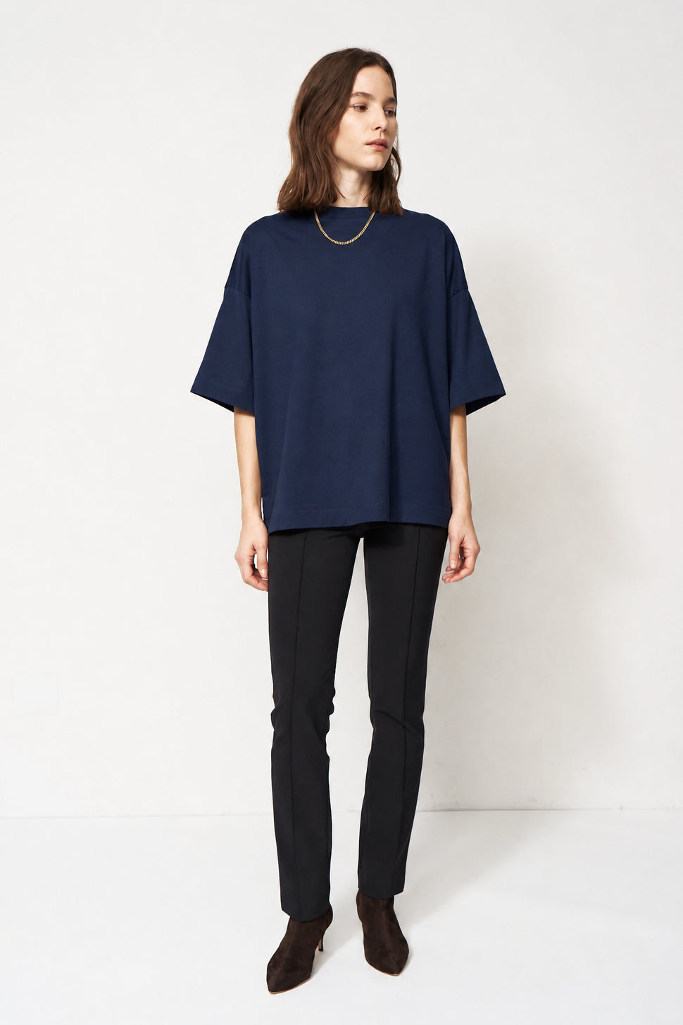 A woman modeling an oversized dark NAVY short-sleeve top with black pants and brown ankle boots, standing against a plain white studio background.