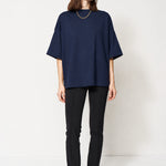 A woman modeling an oversized dark NAVY short-sleeve top with black pants and brown ankle boots, standing against a plain white studio background.