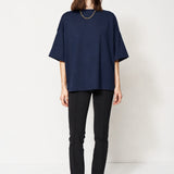 A woman modeling an oversized dark NAVY short-sleeve top with black pants and brown ankle boots, standing against a plain white studio background.