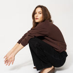 Woman in brown sweater and black pants sitting on a white background