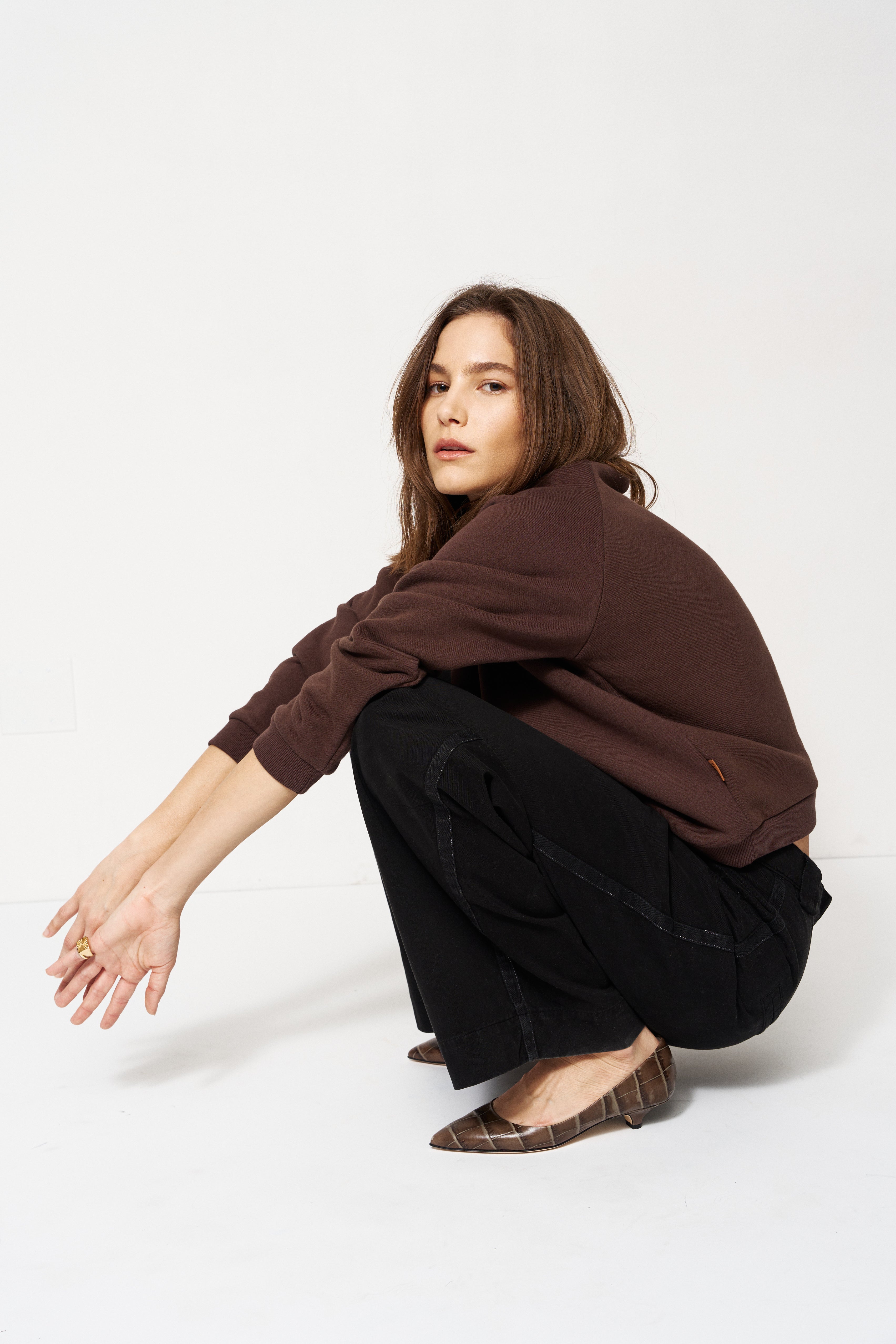 Woman in brown sweater and black pants sitting on a white background