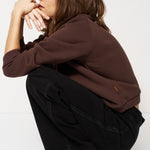 woman in slouch position wearing black pants, kitten heels, and a brown sweater with a white studio background