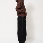 Woman in brown sweater and black pants standing with a white background