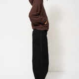 Woman in brown sweater and black pants standing with a white background