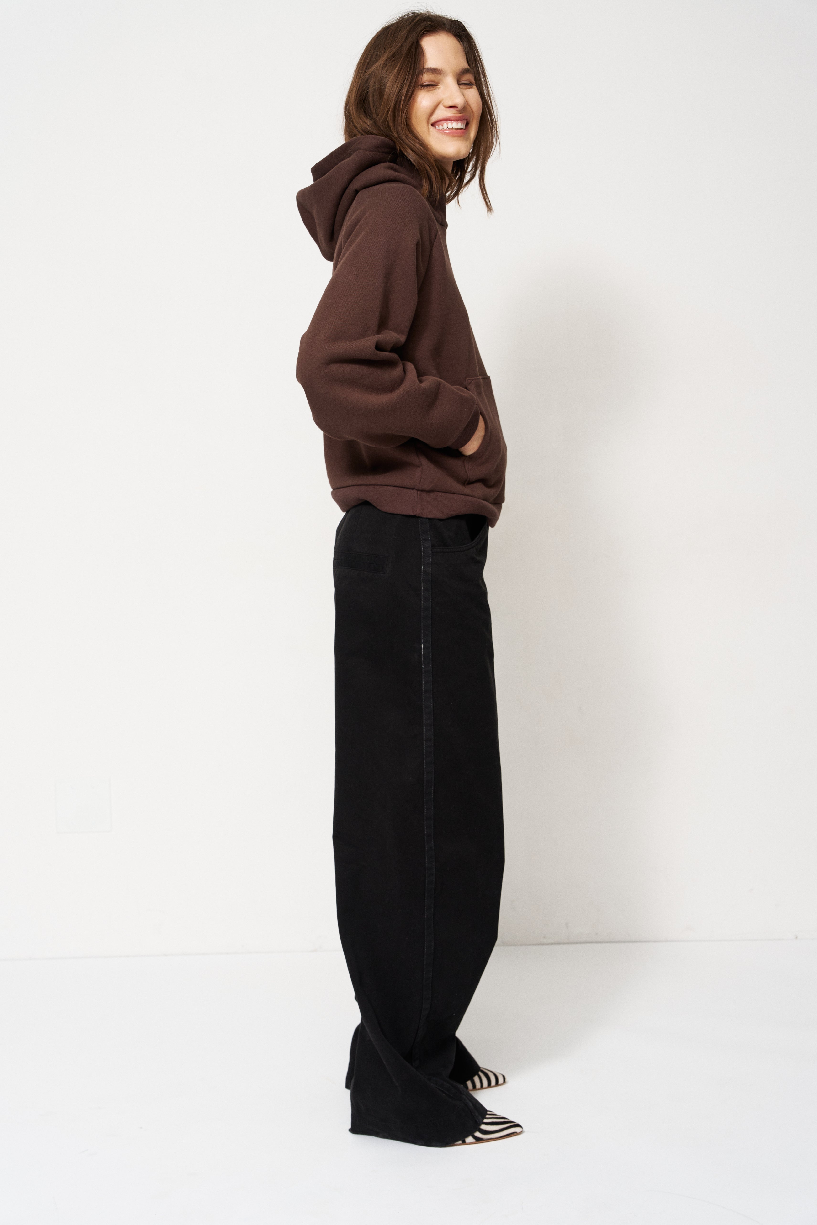 Woman in brown sweater and black pants standing with a white background