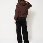 Person wearing a brown hoodie and black pants against a white background