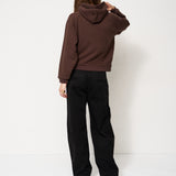 Person wearing a brown hoodie and black pants against a white background
