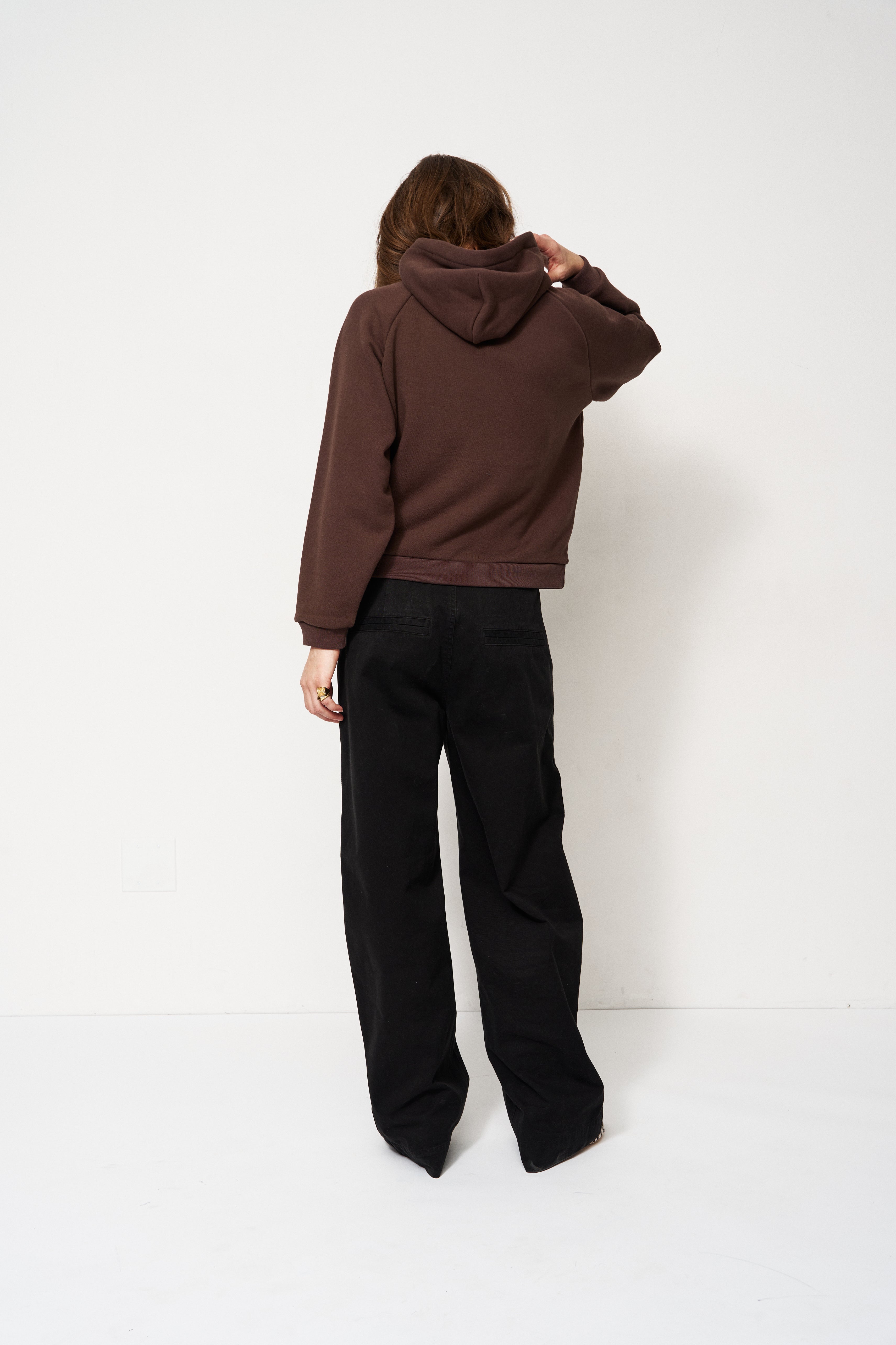 Person wearing a brown hoodie and black pants against a white background