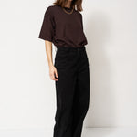 Person wearing a brown top and black pants against a white background