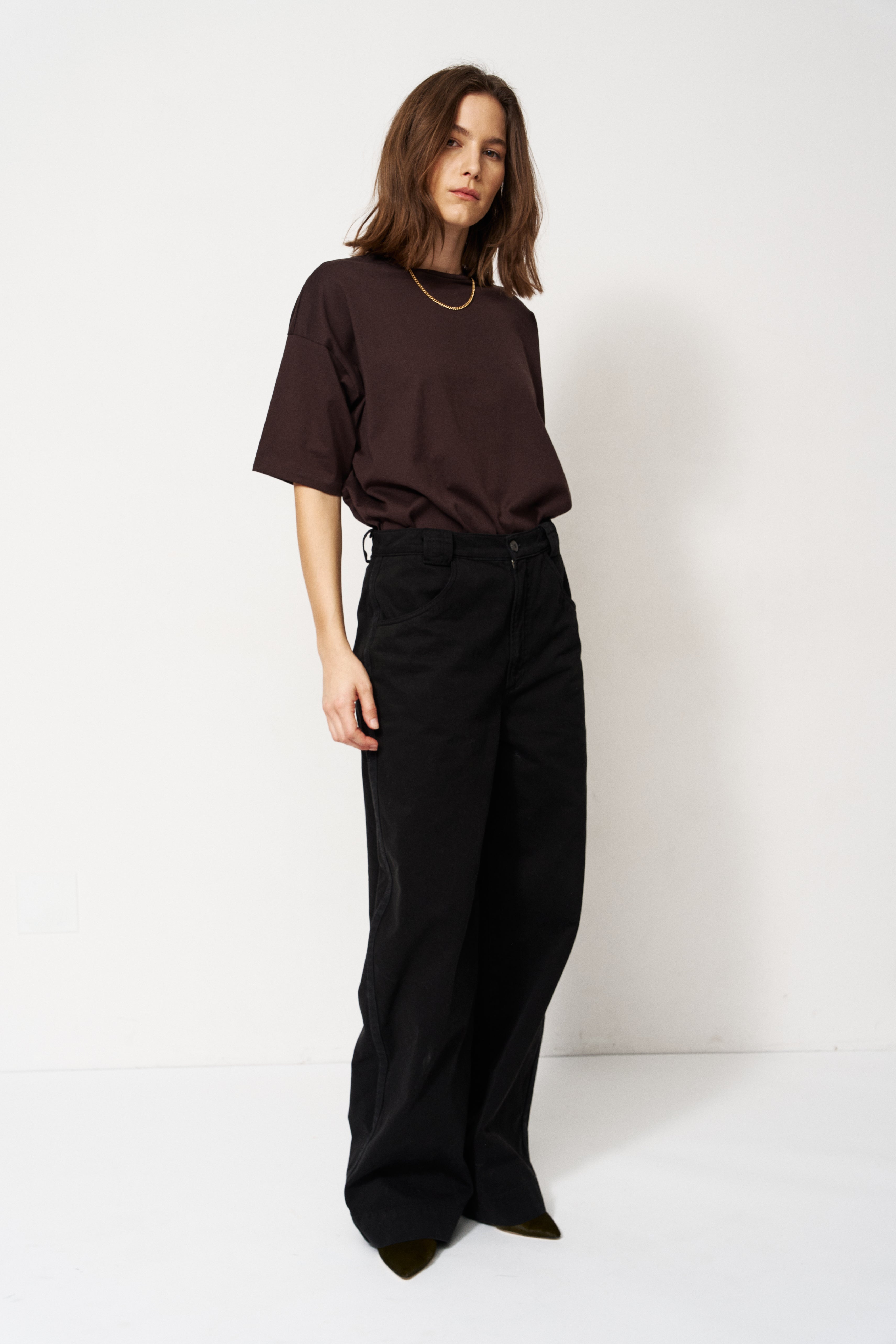 Person wearing a brown top and black pants against a white background