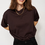 Woman wearing a dark brown t-shirt and black pants against a white background