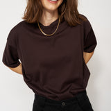 Woman wearing a dark brown t-shirt and black pants against a white background
