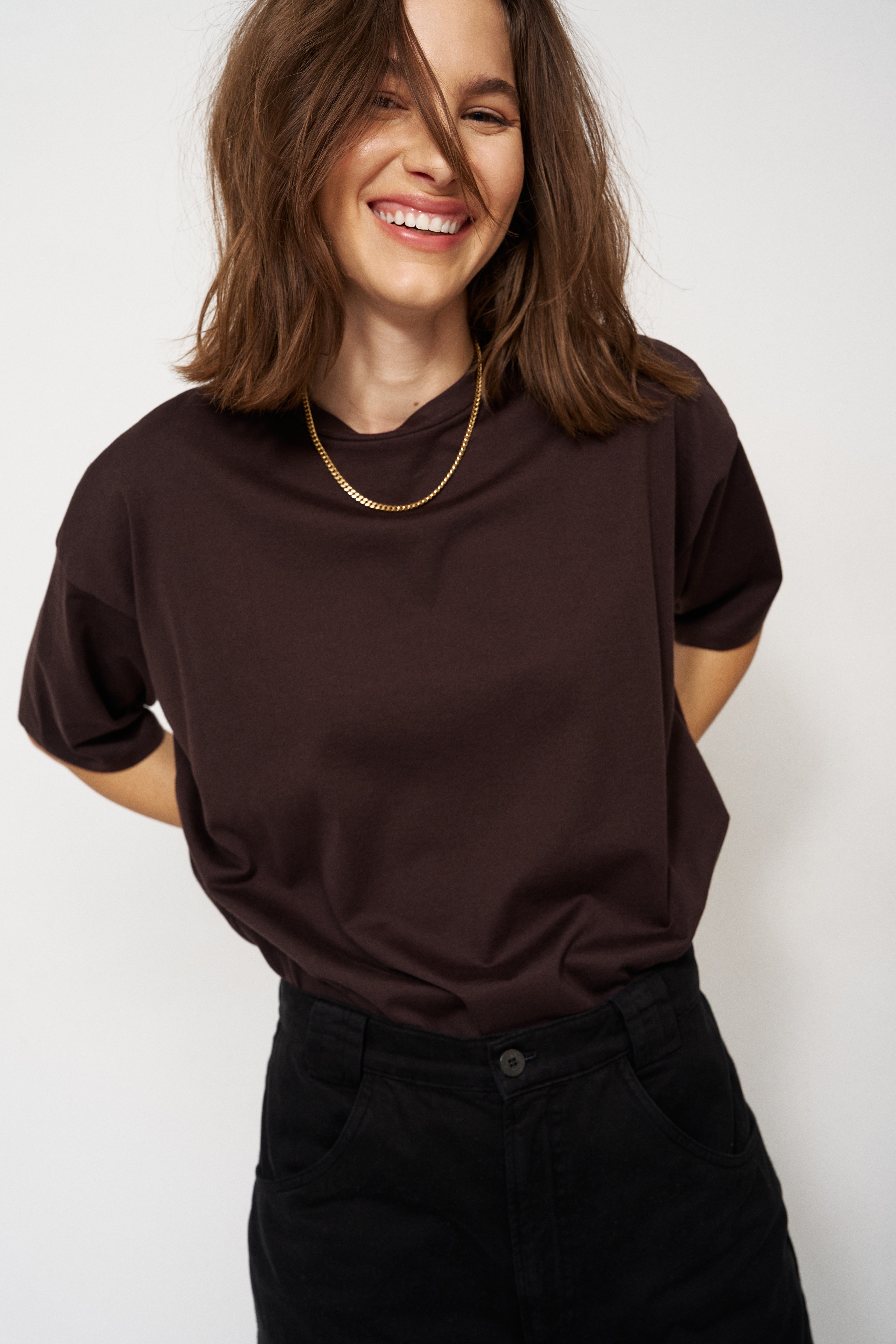 Woman wearing a dark brown t-shirt and black pants against a white background