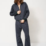 A woman modeling a dark navy blue zip-up jacket and matching wide-leg pants set, paired with brown shoes, against a plain white studio background.