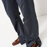 Close-up of a person wearing dark charcoal gray wide-leg trousers with side buttons and brown leather loafers, shown from the knees down against a white studio background.