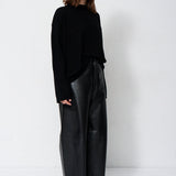 A woman modeling a black long-sleeve knit top and black wide-leg leather pants against a plain white studio background.