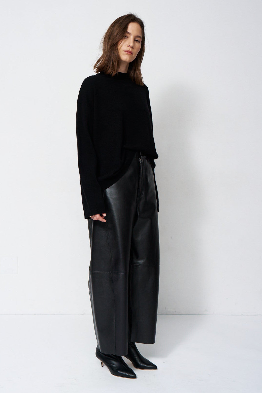 A woman modeling a black long-sleeve knit top and black wide-leg leather pants against a plain white studio background.