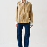 woman in gold striped shirt and jeans againsta a white wall 