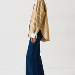 woman in gold striped shirt and jeans againsta a white wall 