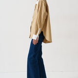 woman in gold striped shirt and jeans againsta a white wall 