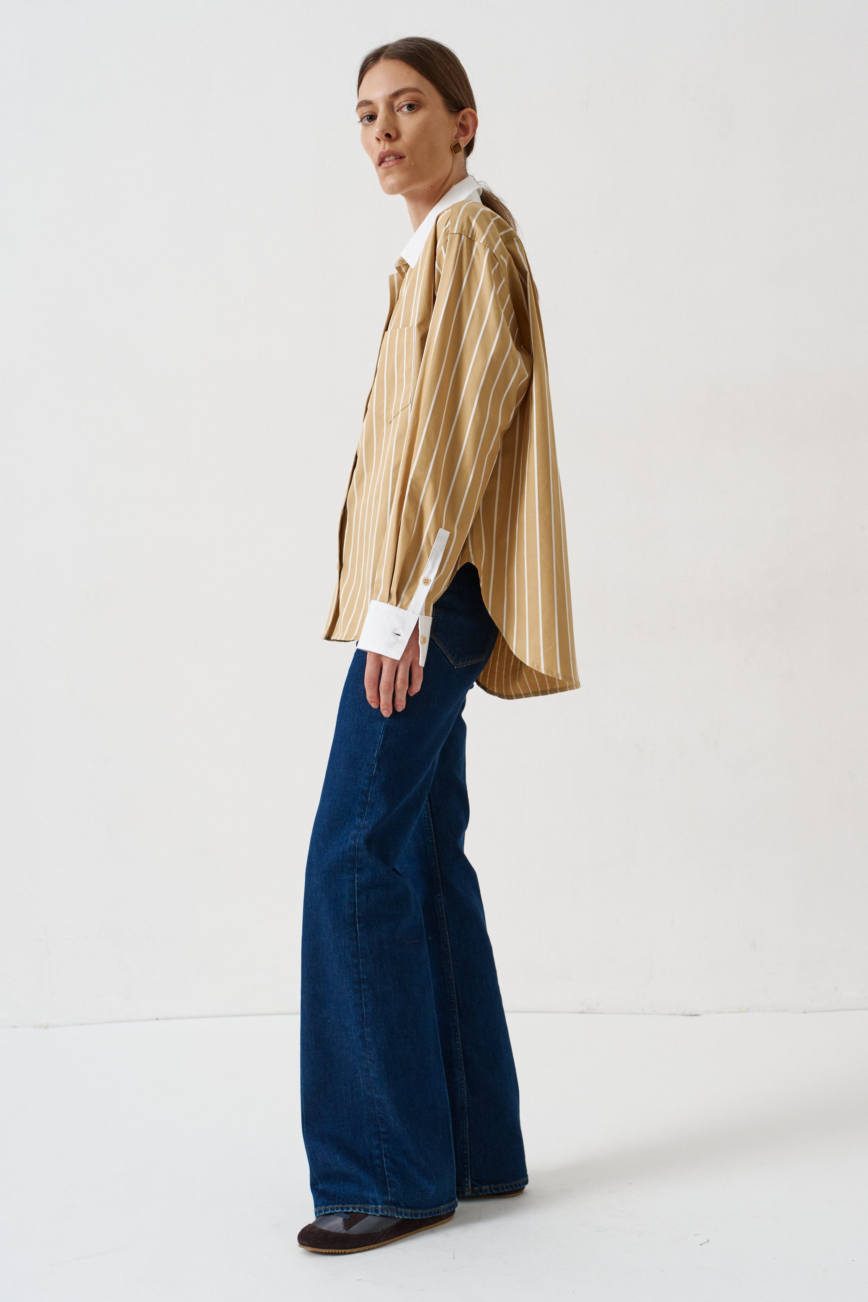 woman in gold striped shirt and jeans againsta a white wall 