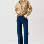 woman in gold striped shirt and jeans againsta a white wall 