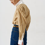woman in gold striped shirt and jeans againsta a white wall 