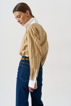 woman in gold striped shirt and jeans againsta a white wall 