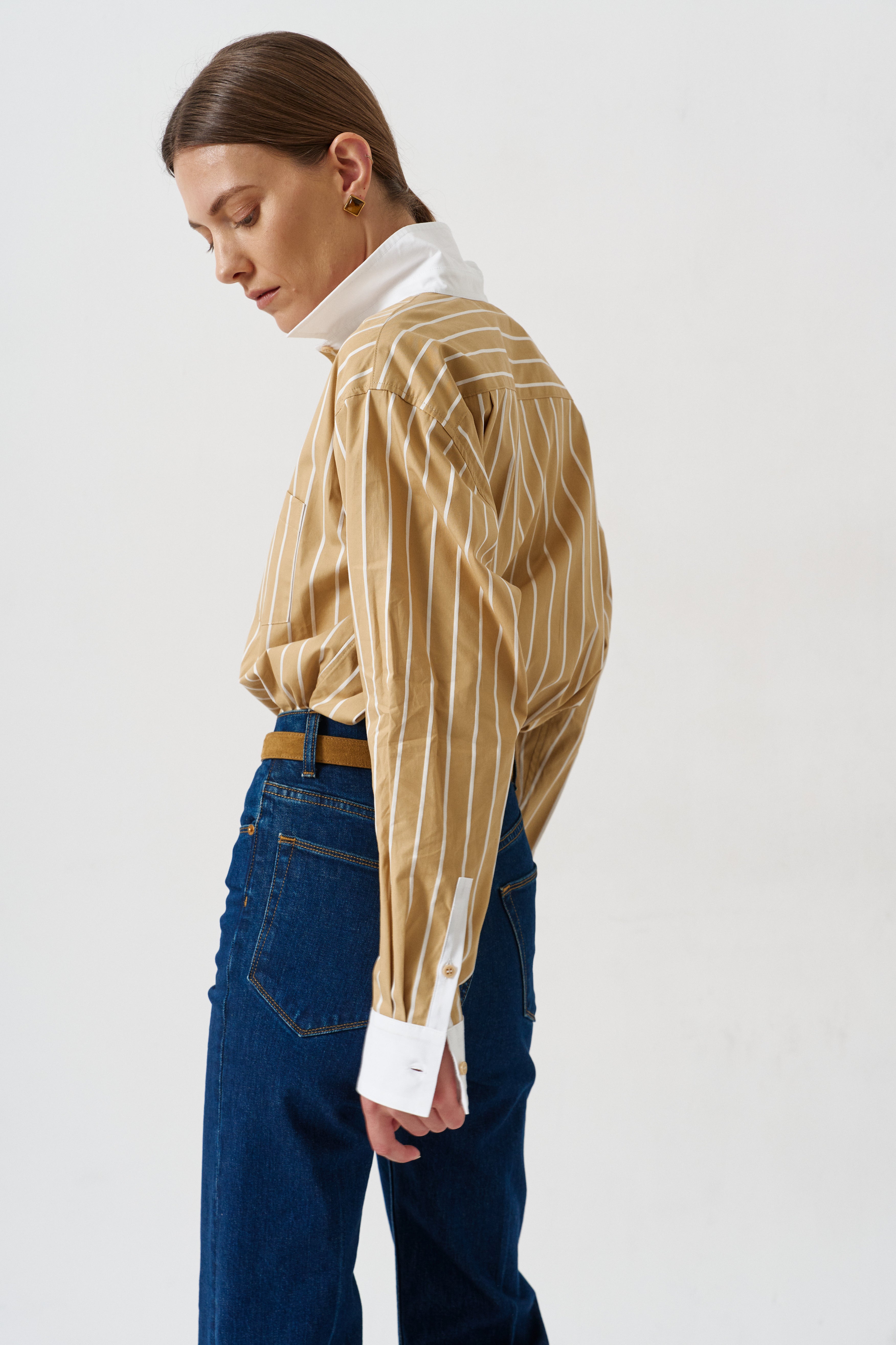 woman in gold striped shirt and jeans againsta a white wall 