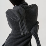 A person shown from the back wearing a dark charcoal gray ribbed knit sweater with oversized draped sleeves, photographed against a plain light background.