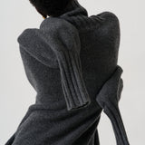 A person shown from the back wearing a dark charcoal gray ribbed knit sweater with oversized draped sleeves, photographed against a plain light background.