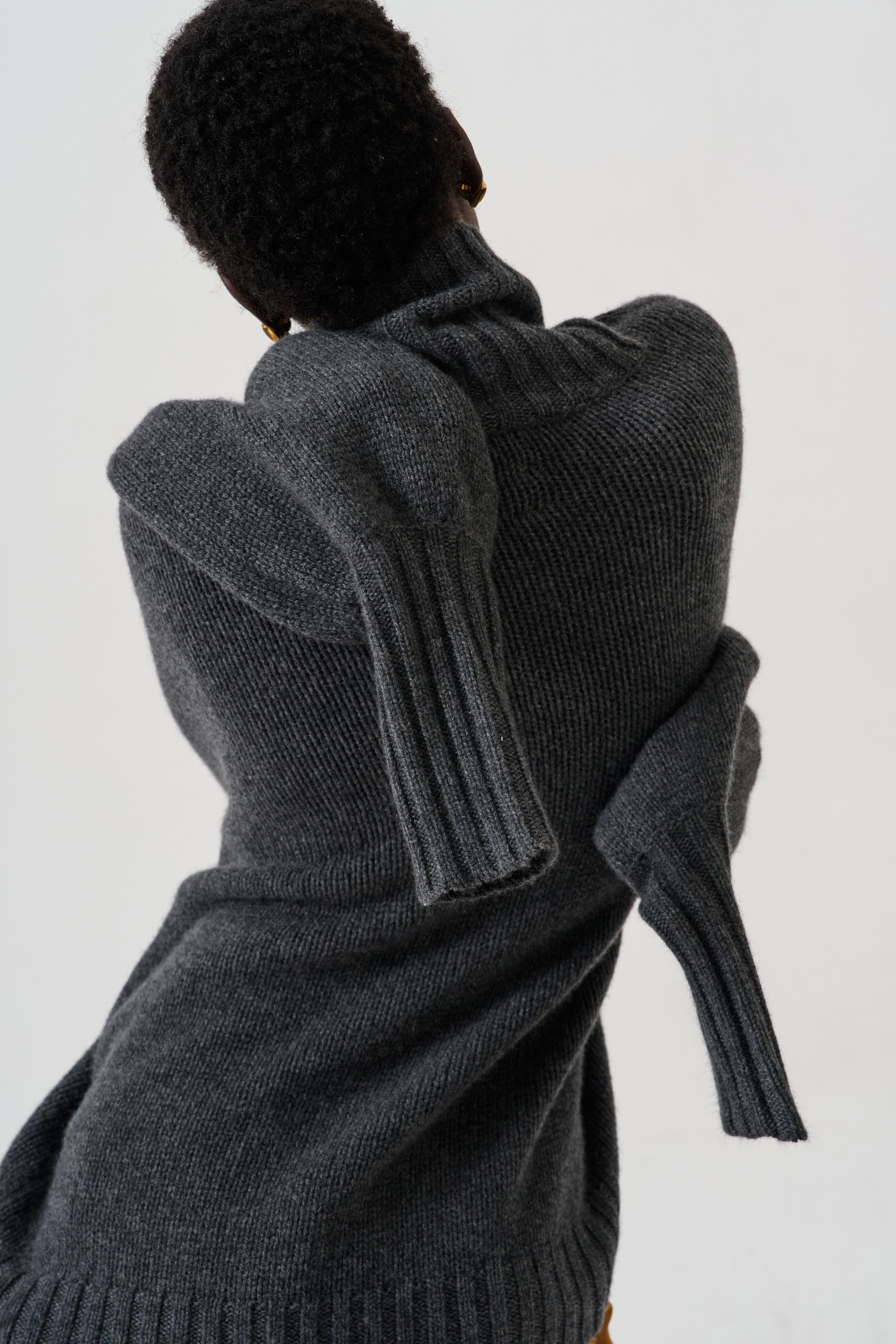 A person shown from the back wearing a dark charcoal gray ribbed knit sweater with oversized draped sleeves, photographed against a plain light background.