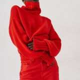 A model wearing a vibrant red oversized turtleneck sweater and matching red trousers, posed against a clean white studio background.