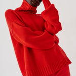 A model wearing a vibrant red knit turtleneck sweater and matching red trousers, posing against a light gray studio background.