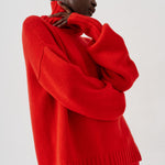 A model wearing a bright red knit sweater and matching red trousers, shown from the side against a plain light gray studio background.