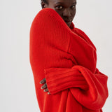 A model wearing a vibrant red chunky knit sweater, wrapped around their body, photographed against a clean white studio background.