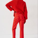 A model shown from the back wearing a bright red knit turtleneck sweater and matching red trousers, paired with brown shoes, against a clean white studio background.