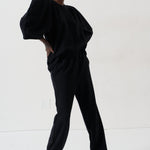 A model wearing a black two-piece lounge set consisting of a loose-fitting top with voluminous sleeves and matching wide-leg pants, styled with patterned shoes against a plain white studio background.