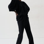 A model wearing a black two-piece lounge set consisting of a loose-fitting top with voluminous sleeves and matching wide-leg pants, styled with patterned shoes against a plain white studio background.