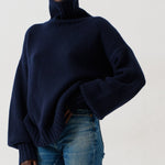 A model wearing a dark navy blue turtleneck sweater, blue cropped jeans, and dark slip-on shoes, standing against a plain white studio background.