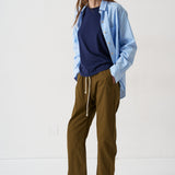 Woman wearing a blue shirt over a navy top with brown pants on a white background
