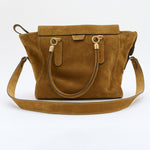 A tan suede handbag with gold-tone hardware, featuring dual top handles and a detachable shoulder strap, photographed against a plain white background.