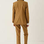 A model viewed from behind wearing a camel brown tailored suit, consisting of a blazer and matching trousers, paired with beige loafers against a plain white studio background.