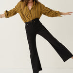 A woman modeling a mustard yellow and black striped long-sleeve button-up shirt paired with black flared pants, posed against a clean off-white studio background.
